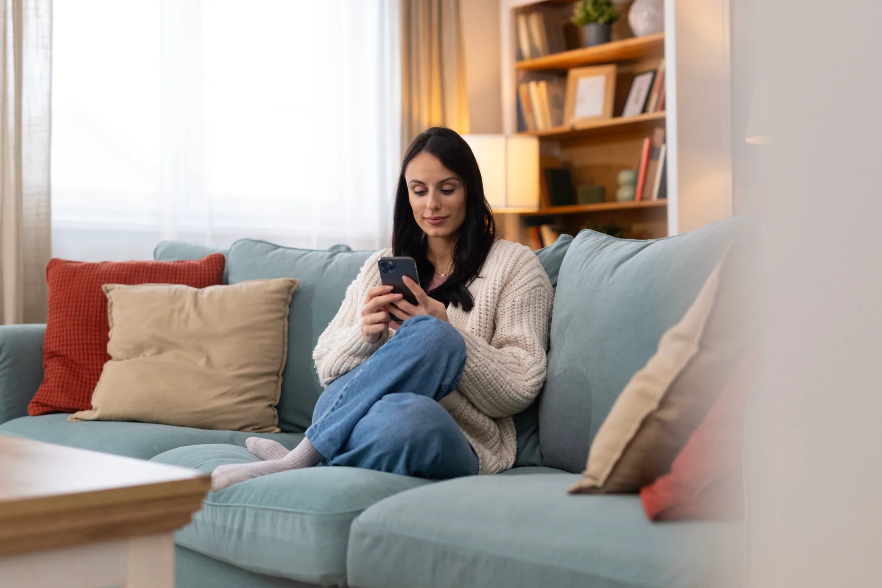 Woman on the couch looking at her phone in warm lamplight